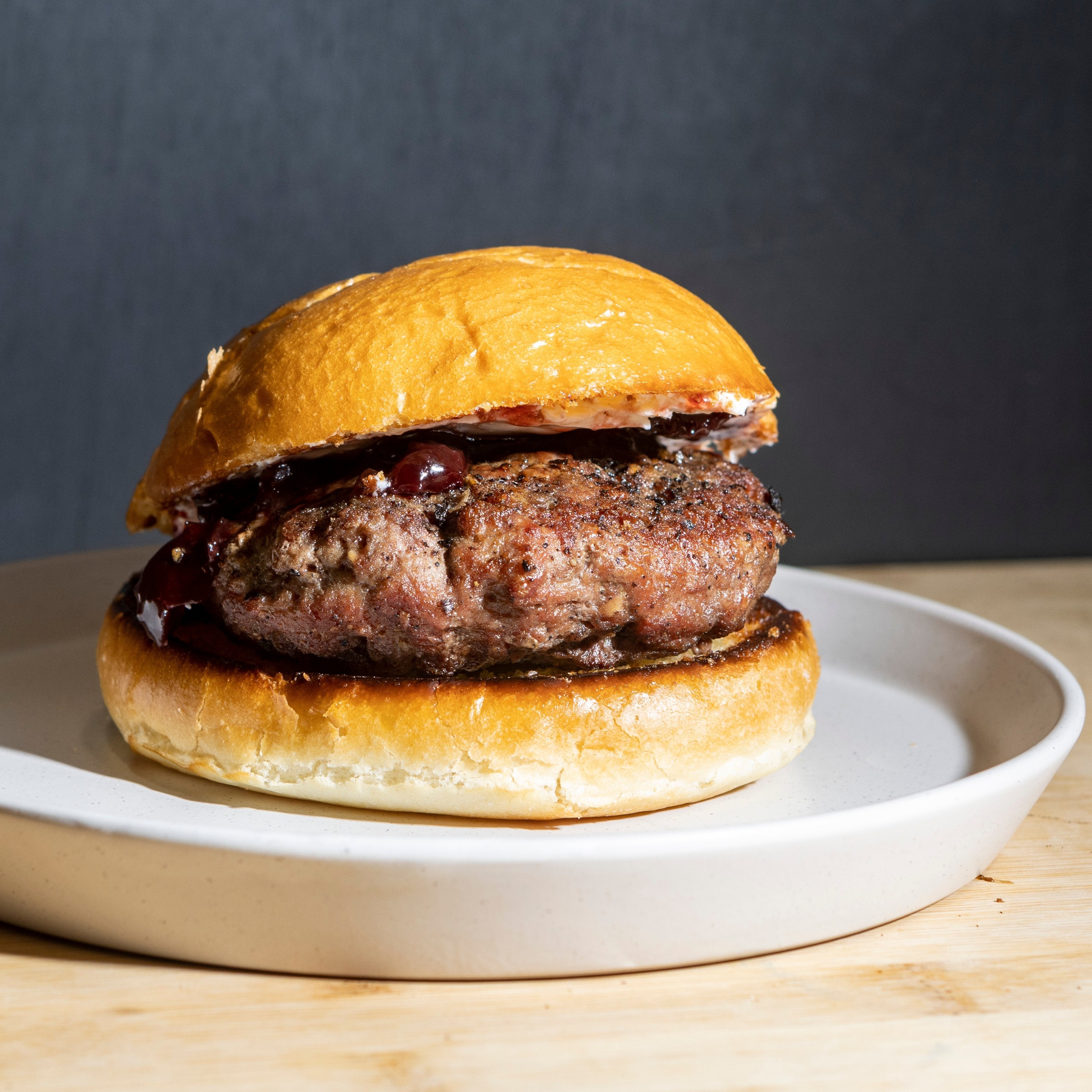 A thick ground lamb burger on a brioche bun garnished with cherry jam, red onion, and cream cheese.